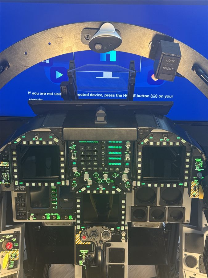 A real F/A-18 cockpit with a hand controller (LOCK/SHOOT grip) clamped to the canopy arch above the instrument panel - a fixed, rig-mounted reference controller.